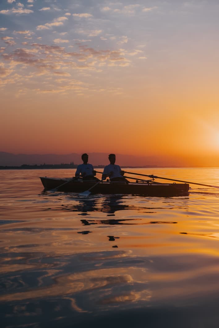 Two rowers silhouetted on a calm lake at sunset